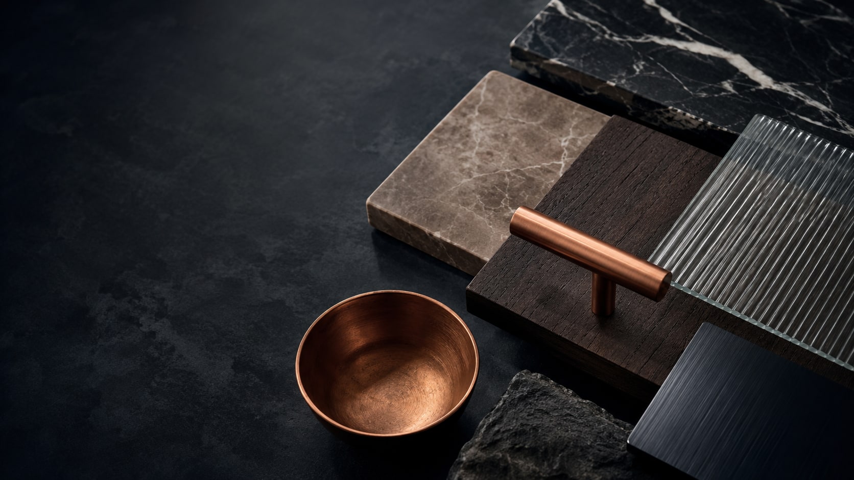 Natural stone, dark wood, fluted glass and metal finish samples arranged on a charcoal surface.